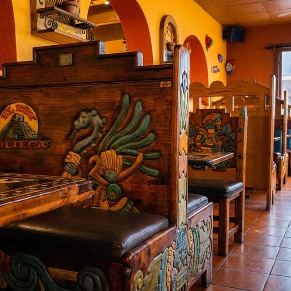 Restaurant interior with ornate wooden booths, orange walls, and an "OPEN" sign visible through the front door.