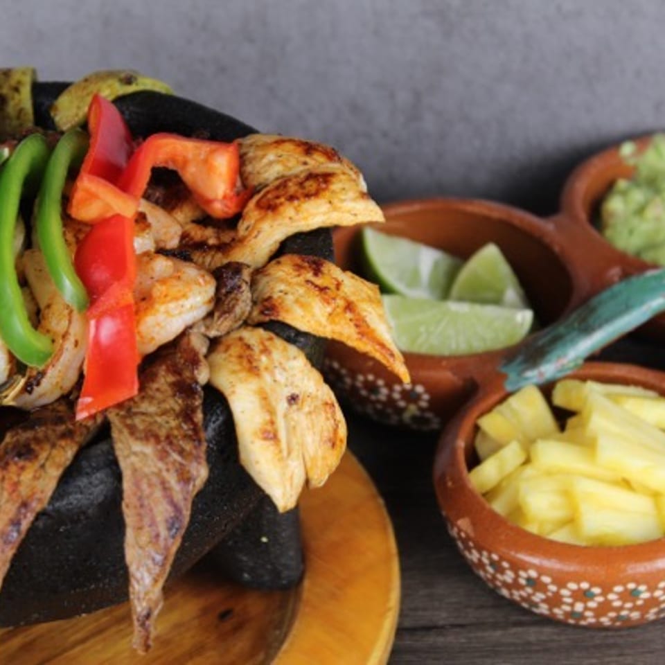 Grilled chicken and steak fajitas with peppers, onions, lime, guacamole, salsa, and pineapple in rustic bowls.